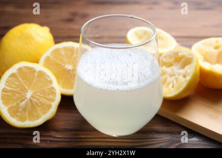 Succo fresco in bicchiere e limoni su tavolo di legno, primo piano Foto Stock