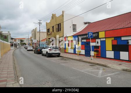 Edifici colorati in stile coloniale vicino al quartiere del centro, con strade strette, palme e alcune auto parcheggiate a Oranjestad ad Aruba. Foto Stock