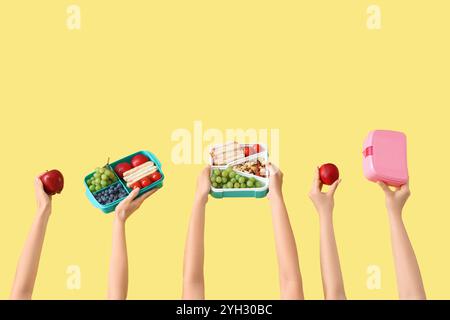 Mani femminili con cestini per pranzo scolastici e frutta su sfondo giallo Foto Stock