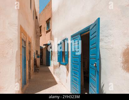 Stradina tortuosa nella Medina, Essaouira, Marocco, con iconiche porte e persiane blu, tradizionali edifici rustici della città vecchia Foto Stock