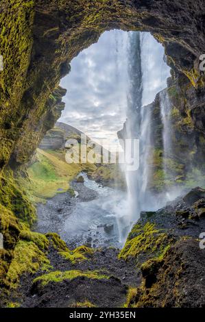 Vista da dietro la cascata Kvernufoss in Islanda, che mostra una gemma nascosta con muschio verde lussureggiante, aspre formazioni rocciose e una cascata Foto Stock