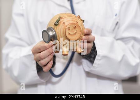 Medico che tiene il salvadanaio da vicino. Concetto di assicurazione medica e di denaro per l'assistenza sanitaria Foto Stock