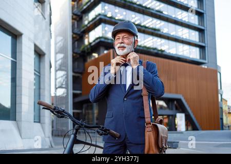 Ritratto di un uomo d'affari con la barba che indossa il casco da ciclista mentre è in piedi in bicicletta in città Foto Stock