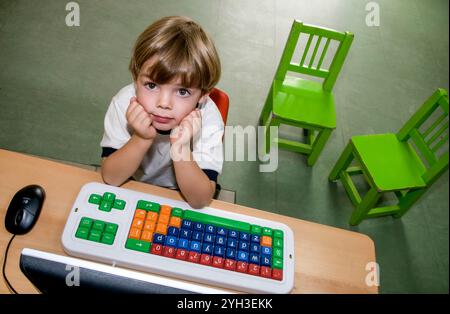 Computer e bambino biondo bambino di 4 anni, scuola elementare dell'asilo, guarda in alto dal suo computer didattico, mouse e tastiera Foto Stock
