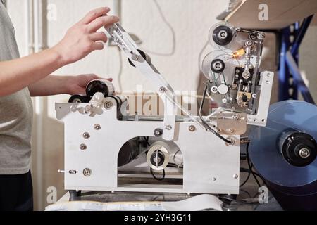 Shot ritagliato di un operaio di fabbrica maschio che applica etichette sulle bottiglie utilizzando l'etichettatrice degli adesivi presso la linea di produzione dell'impianto di produzione di sidro artigianale, spazio di copia Foto Stock