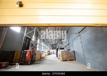 Vista interna del magazzino con scaffali, pallet e un carrello elevatore sotto un soffitto strutturato. Foto Stock