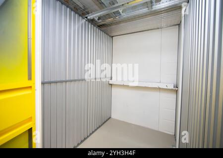 Aprire lo sportello giallo che rivela un'unità di stoccaggio vuota con pareti metalliche all'interno di una struttura. Foto Stock