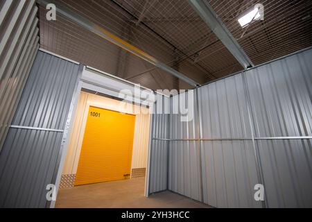 Interno di un vano portaoggetti vuoto con pareti metalliche con vista su una porta arrotolabile gialla. Foto Stock