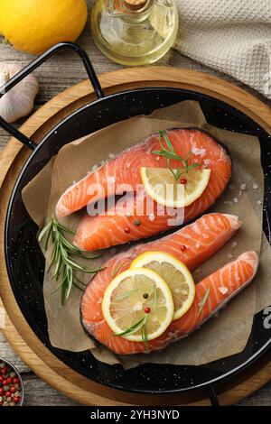 Bistecche di salmone crude fresche con spezie in padella e prodotti su tavola di legno, piatti Foto Stock