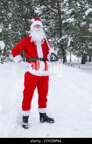 Babbo Natale pulisce la neve con la pala in inverno all'aperto dopo una nevicata. Pulire le strade del villaggio, pulire il passaggio per le auto, difficile Foto Stock