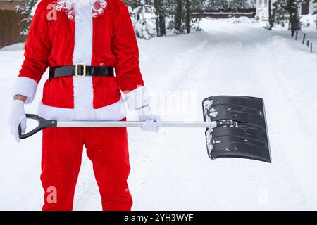 Babbo Natale pulisce la neve con la pala in inverno all'aperto dopo una nevicata. Pulire le strade del villaggio, pulire il passaggio per le auto, difficile Foto Stock