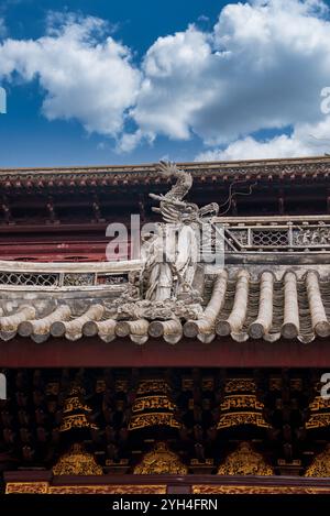 Il tetto tradizionale cinese a Shanghai, con dettagli intricati, presenta intagli ornati e una mitica scultura, adagiata su un cielo blu chiaro. Foto Stock