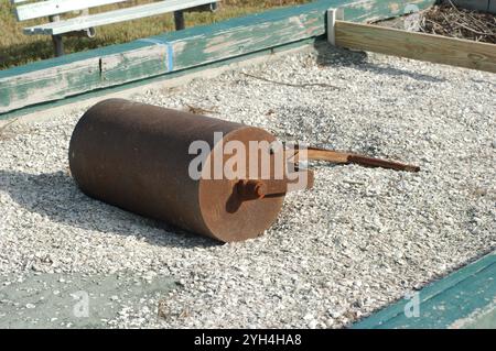 Vista laterale Rusty Brown Metal Lawn Roller sul campo da bocce Ball che è stato spazzato via dall'uragano Helene e dall'uragano Milton. Marciapiede e ponte in legno l Foto Stock