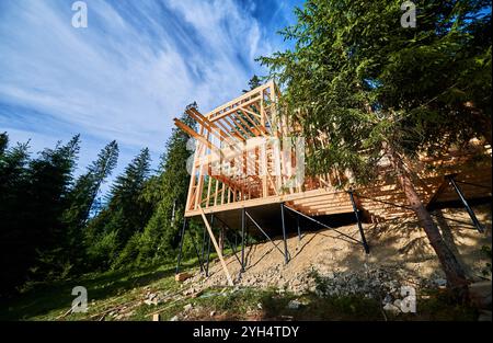 Edificio residenziale con struttura in legno in corso di costruzione vicino a una foresta. Inizio della nuova costruzione di un comodo cottage. Idea di costruzione ecologica, design architettonico contemporaneo Foto Stock