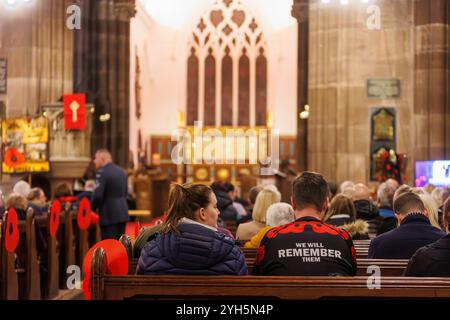 Warrington, Cheshire, Inghilterra, Regno Unito. 9 novembre 2024. Il Festival annuale della memoria si svolge all'interno della chiesa parrocchiale di St Elphin. Era una serata per ricordare e onorare il servizio e il sacrificio delle nostre forze armate nei conflitti mondiali. L'uomo che indossa una camicia con i papaveri e "li ricorderemo" siede a lato della chiesa per il servizio. Crediti: John Hopkins/Alamy Live News Foto Stock