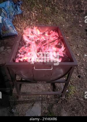 Braci accesi e carboni caldi preparati per un barbecue all'aperto. Il calore intenso e le scintille creano un'atmosfera rustica e invitante per la cottura alla griglia. Foto Stock