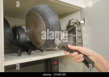 Mano che serve la padella sul ripiano della cucina con vari utensili e grattugia sullo sfondo. Primo piano nel concetto di organizzazione dello stoccaggio in cucina. Foto Stock