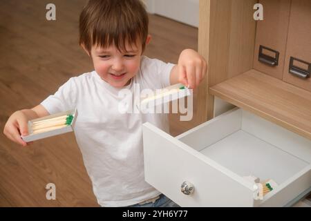 Un bambino tiene in mano un fiammifero illuminato, che è altamente infiammabile e rischioso. Il bambino sta pericolosamente giocando con una fiamma all'interno della casa. Ragazzo invecchiato Foto Stock