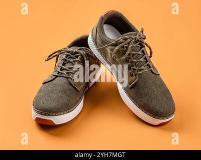 Scarpe allacciate in tela cachi su sfondo arancione. Un paio di nuove scarpe in tessuto marrone con suola bianca per uno stile di vita attivo, fitness e sport. Foto Stock