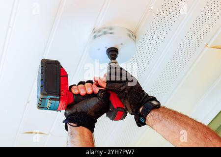 Un singolo guanto può contenere trapani senza fili con attacco per sega a tazza, taglia fori circolari nel soffitto bianco per alloggiare nuovi apparecchi di illuminazione Foto Stock