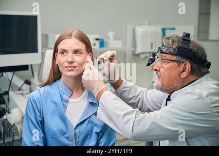 Medico adulto che utilizza uno strumento medico per ispezionare l'orecchio Foto Stock