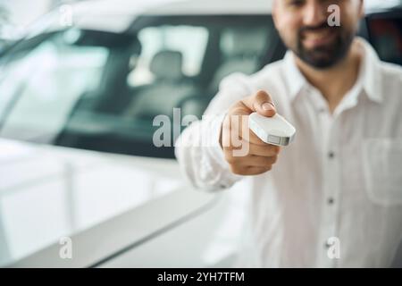Uomo sorridente che mostra la chiave della vettura allo showroom della concessionaria Foto Stock