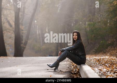 Una donna elegante seduta sul marciapiede in un ambiente della foresta autunnale. Foto Stock