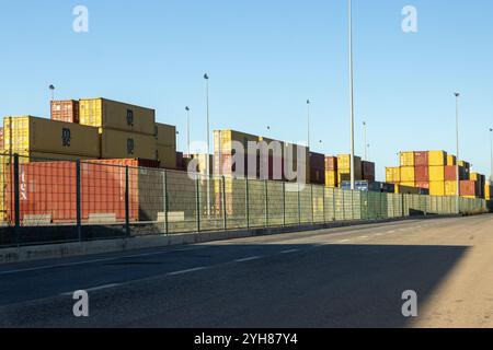 I coloratissimi container sono impilati in alto dietro una recinzione di sicurezza in un terminal portuale, in attesa del trasporto e dimostrando il commercio globale Foto Stock