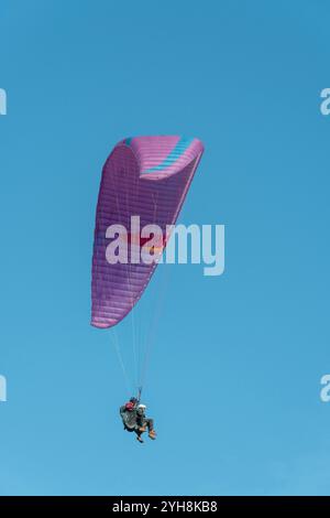 I parapendio tandem si innalzano in alto sopra il paesaggio sotto una vivace tettoia rosa in una giornata limpida e soleggiata Foto Stock