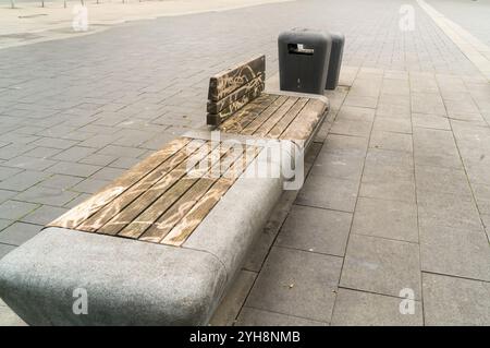 Bagnare la panchina in legno con graffiti vicino a due bidoni della spazzatura in una piazza deserta dopo la pioggia Foto Stock