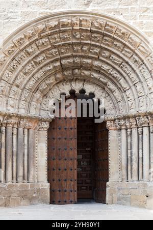 Un arco in pietra splendidamente intagliato incornicia le grandi porte in legno di un'antica chiesa di Obanos, che mostra intricata maestria artigianale. Foto Stock