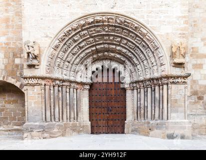 Un arco in pietra splendidamente intagliato incornicia le grandi porte in legno di un'antica chiesa di Obanos, che mostra intricata maestria artigianale. Foto Stock