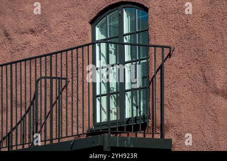 La robusta ringhiera nera conduce ad una grande ed elegante finestra collocata all'interno di una parete rosa testurizzata. La luce del sole riempie lo spazio, evidenziando l'architettura Foto Stock