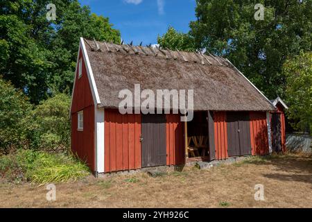 Un affascinante cottage rosso con tetto in paglia sorge in un tranquillo ambiente rurale, circondato da una vegetazione lussureggiante in una giornata di sole Foto Stock