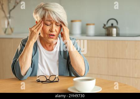 Mal di testa. Donna anziana infelice di mezza età che soffre di mal di testa malata che sfrega le tempie a casa. Anziana nonna anziana matura che tocca i templi che sperimenta stress donna che sente dolore alla testa Foto Stock