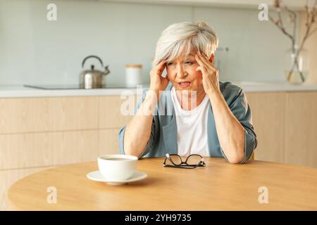 Mal di testa. Donna anziana infelice di mezza età che soffre di mal di testa malata che sfrega le tempie a casa. Anziana nonna anziana matura che tocca i templi che sperimenta stress donna che sente dolore alla testa Foto Stock