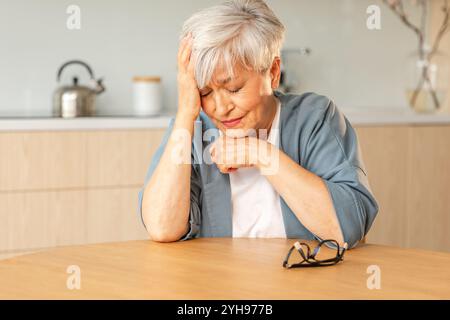 Mal di testa. Donna anziana infelice di mezza età che soffre di mal di testa malata che sfrega le tempie a casa. Anziana nonna anziana matura che tocca i templi che sperimenta stress donna che sente dolore alla testa Foto Stock