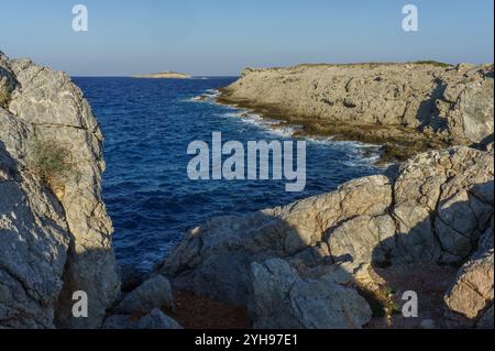 Le onde si infrangono contro scogliere scoscese, creando un'atmosfera serena mentre il sole inizia a tramontare lungo la costa. Foto Stock