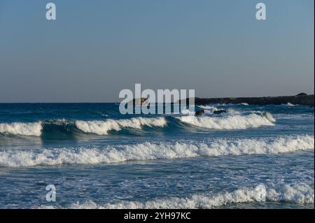 Onde morbide danzano sulla riva, riflettendo le sfumature dorate del tramonto in una posizione tranquilla sulla spiaggia. Foto Stock