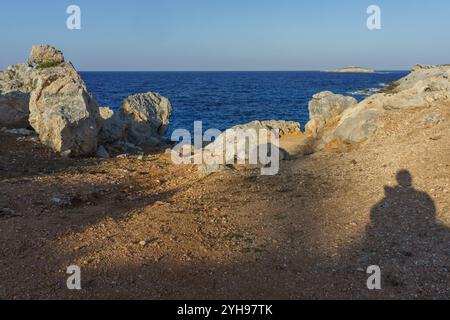 Un sentiero roccioso scende verso l'oceano calmo, con dolci onde che si infrangono contro la riva mentre la sera si avvicina. Foto Stock