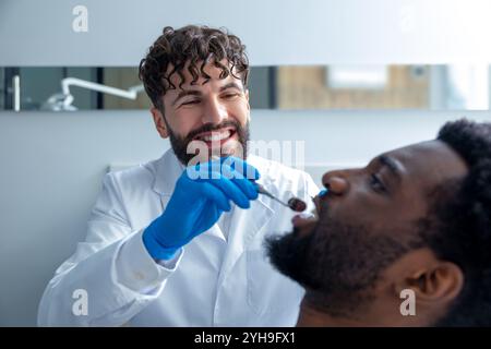 Dentista maschio che ispeziona i denti del paziente con lo specchio fornendo un trattamento essenziale durante il check-up Foto Stock