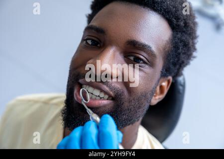 Dentista maschio che ispeziona i denti del paziente con lo specchio fornendo un trattamento essenziale durante il check-up Foto Stock