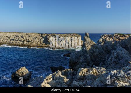 Le onde si infrangono dolcemente contro una costa frastagliata, inondate di calda luce dorata mentre il giorno passa alla sera. Foto Stock