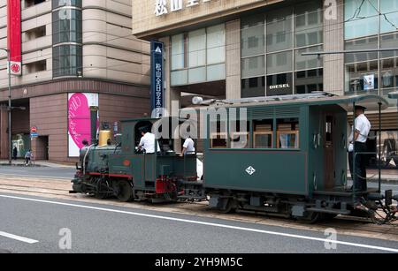 Il vecchio treno locomotivo Botchan Ressha che attraversa le strade di Matsuyama tra la stazione di Matsuyama e Dogo Onsen, Foto Stock