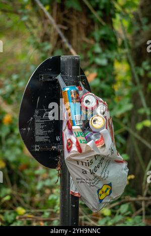 sacco dei rifiuti appeso al cartello stradale pieno di lattine di alluminio usate o vuote per il riciclaggio, sacchetto pieno di lattine usate, raccolta di rifiuti in campagna. Foto Stock