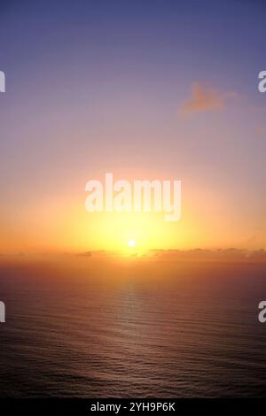 Un tranquillo paesaggio marino che cattura il tramonto sull'oceano. La luce soffusa del sole, appena sopra l'orizzonte, emette toni caldi sull'acqua. Foto Stock