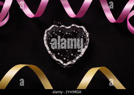 Cuore trasparente in vetro per gioielli. Sfondo nero dei nastri a colori Foto Stock