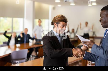 Manager bianco di mezza età che dà il benvenuto a un nuovo dipendente africano Foto Stock