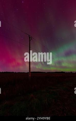 Le linee elettriche si estendono attraverso il paesaggio e si stagliano contro la splendida aurora boreale, evidenziando l'intersezione delle moderne infrastrutture e. Foto Stock