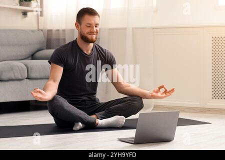 Uomo millenario che medita con il trainer online tramite notebook Foto Stock